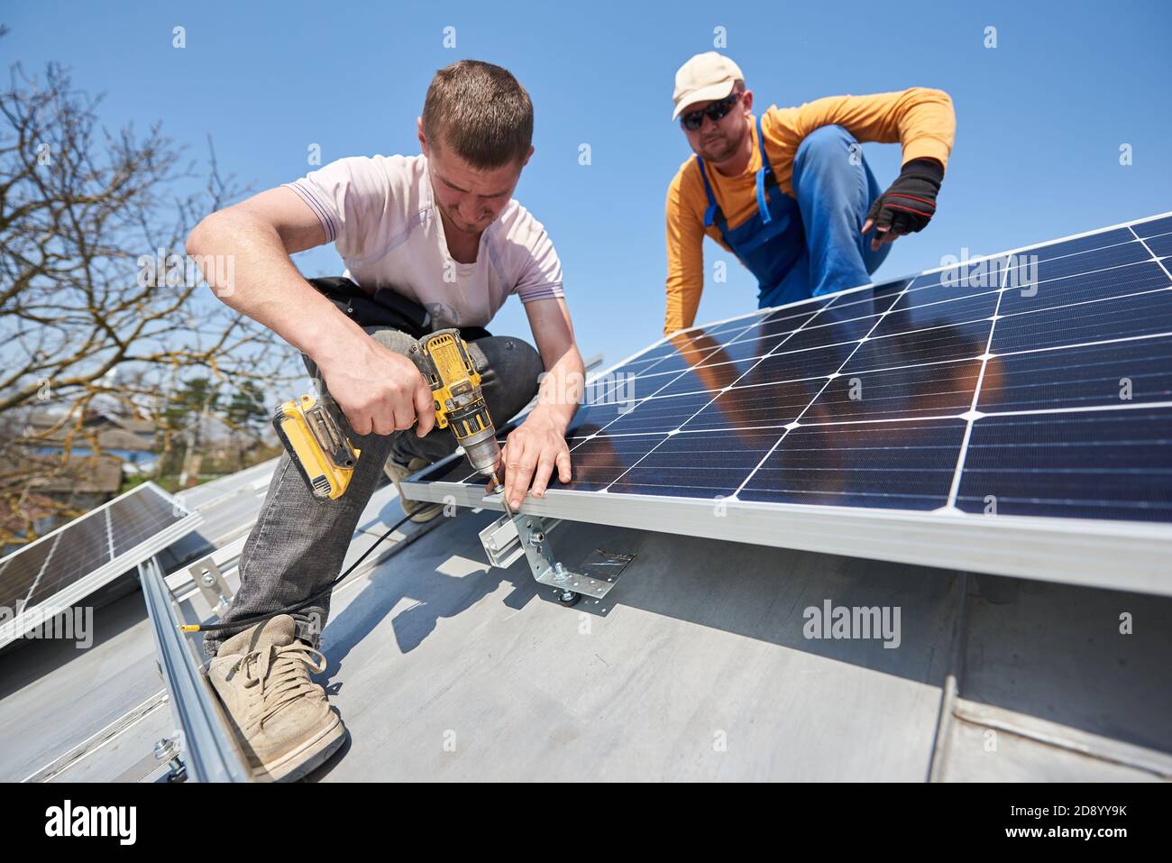 Male engineers installing solar photovoltaic panel system using screwdriver. Two electricians mounting solar module on roof of modern house. Alternative renewable innovation concept. Stock Photo