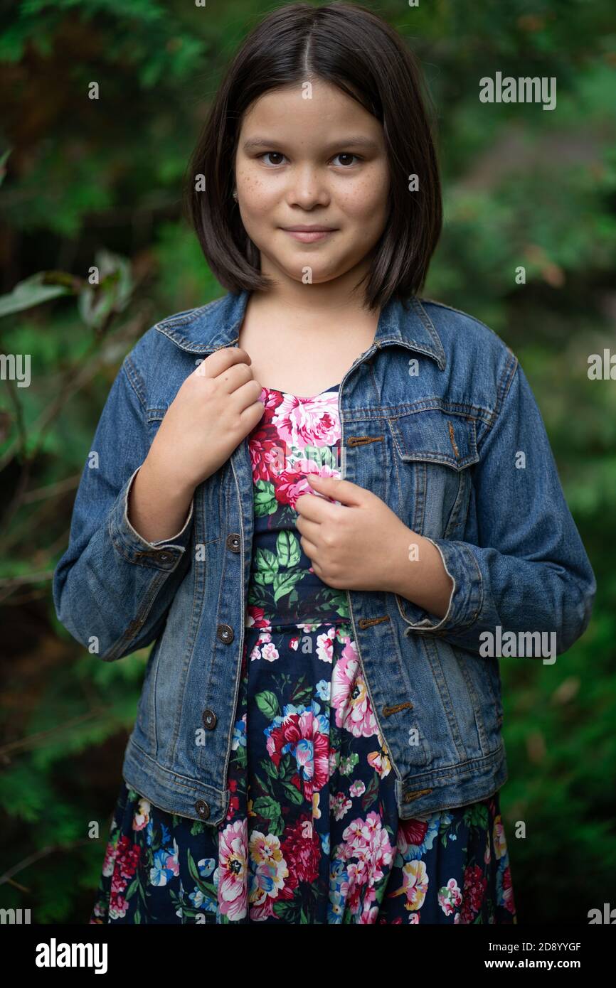 Little Mongolian in colorful sundress and denim jacket with short dark hair posing garden in background Stock Photo