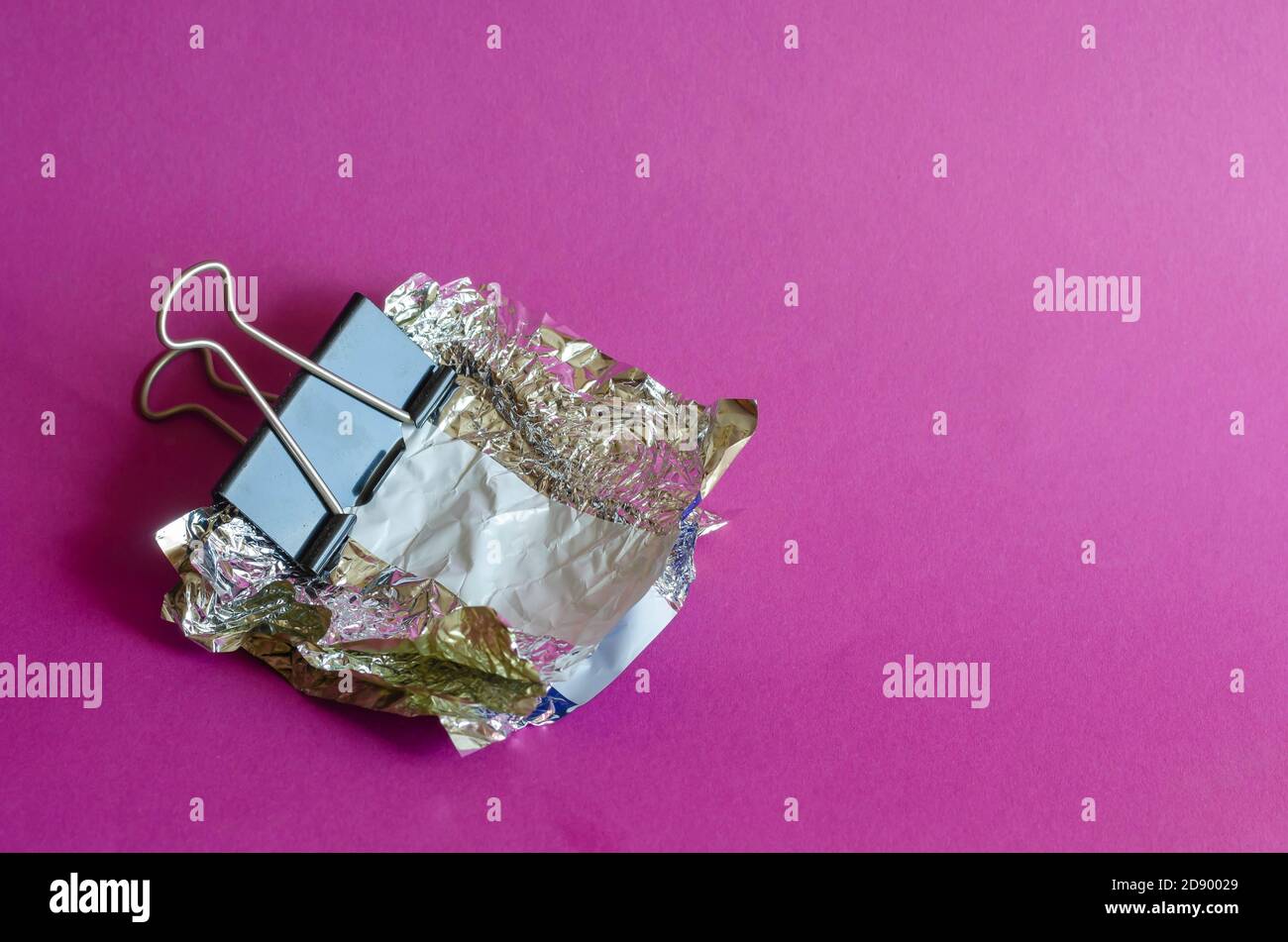 Smashed candy wrappers and Metal black Binder Clip on purple background ...
