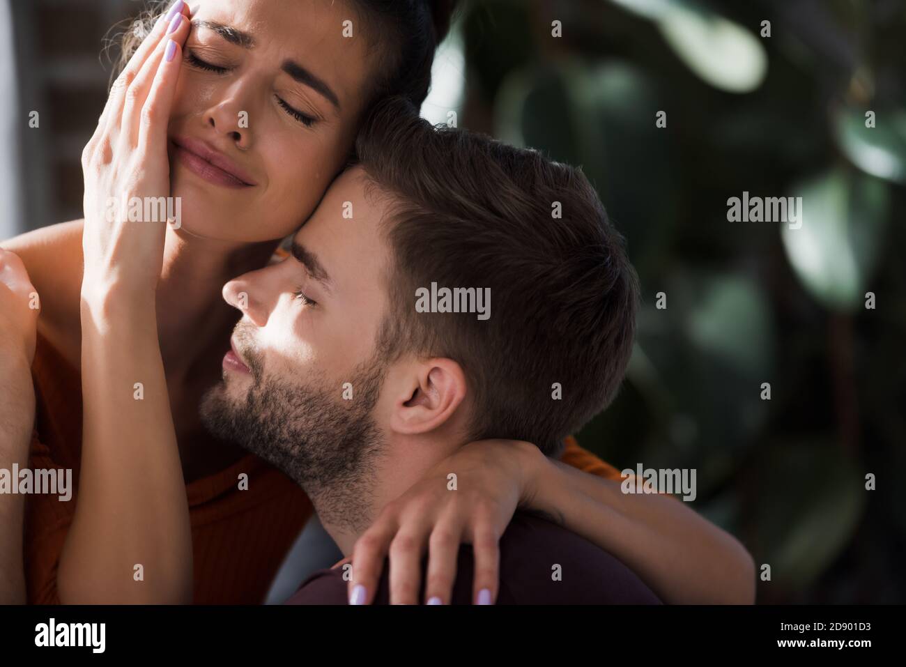 crying woman touching face while embracing beloved man at home Stock Photo