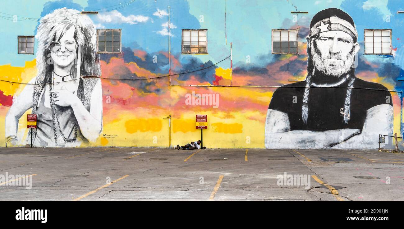 Nothing left to loose, a homeless black man lies in the street in front of a giant mural of Janis Joplin and Willie Nelson. Stock Photo