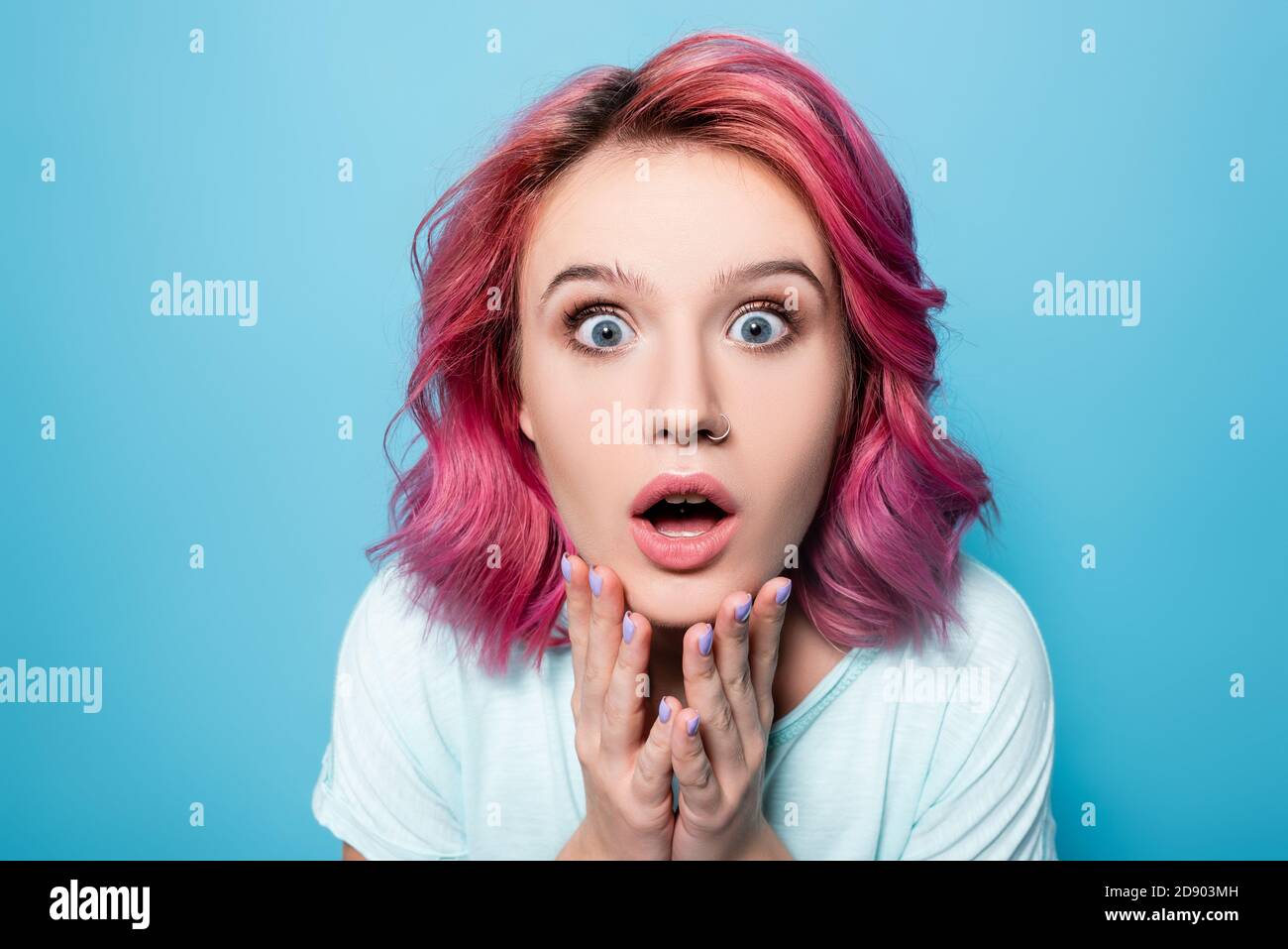 scared young woman with pink hair on blue background Stock Photo