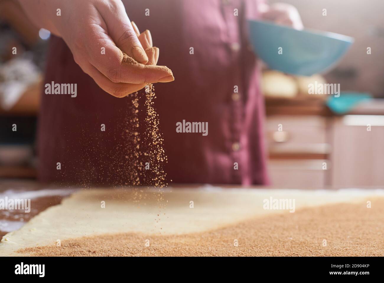 Female hand sprinkles cinnamon on a rolled raw dough for cinnamon buns Stock Photo