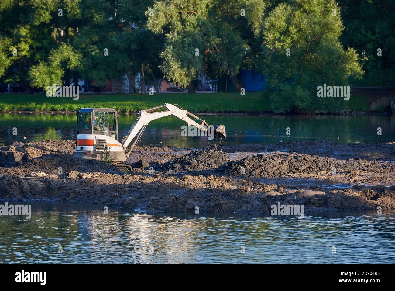 Small excavator cleans the bottom of the pond from silt Stock Photo