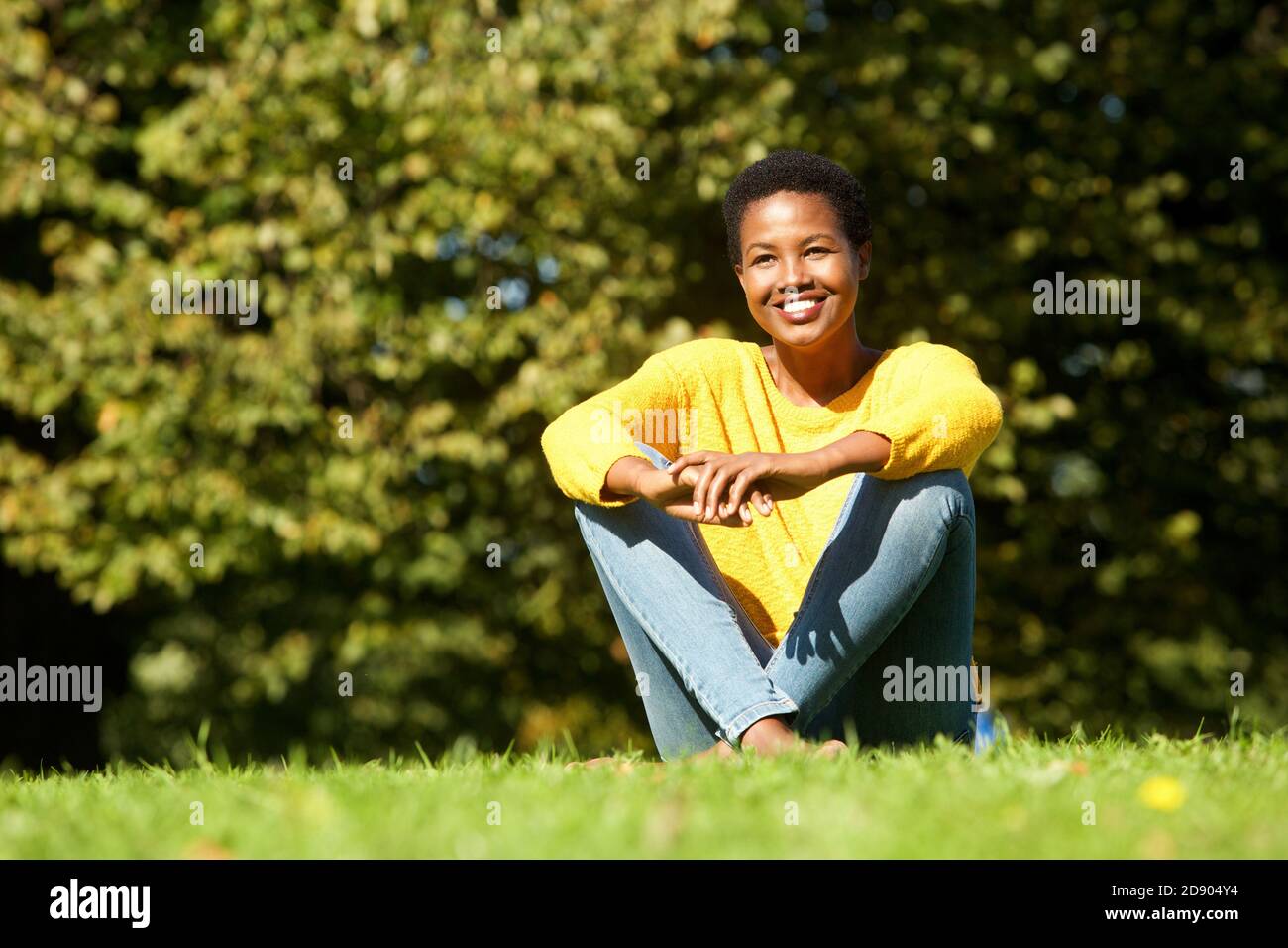 Portrait of happy young black woman sitting on grass outdoor Stock Photo