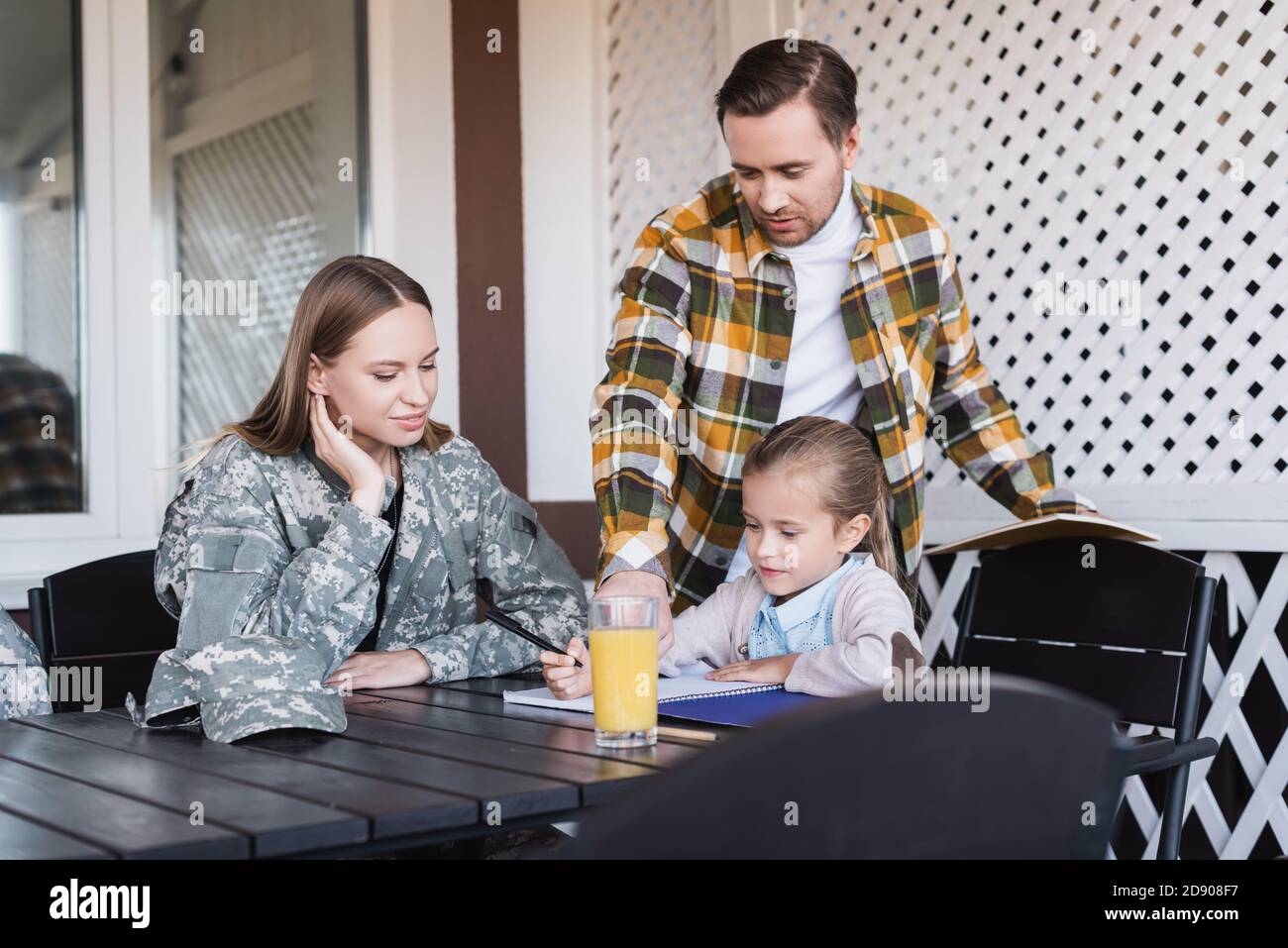 Girl writing at notebook, while sitting near father and mother at home Stock Photo