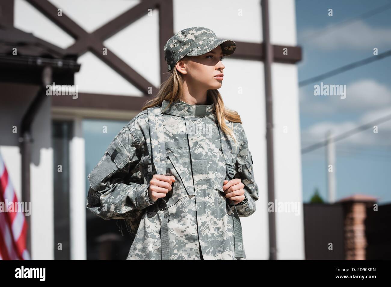 Confident military servicewoman with backpack looking away with blurred house on background Stock Photo