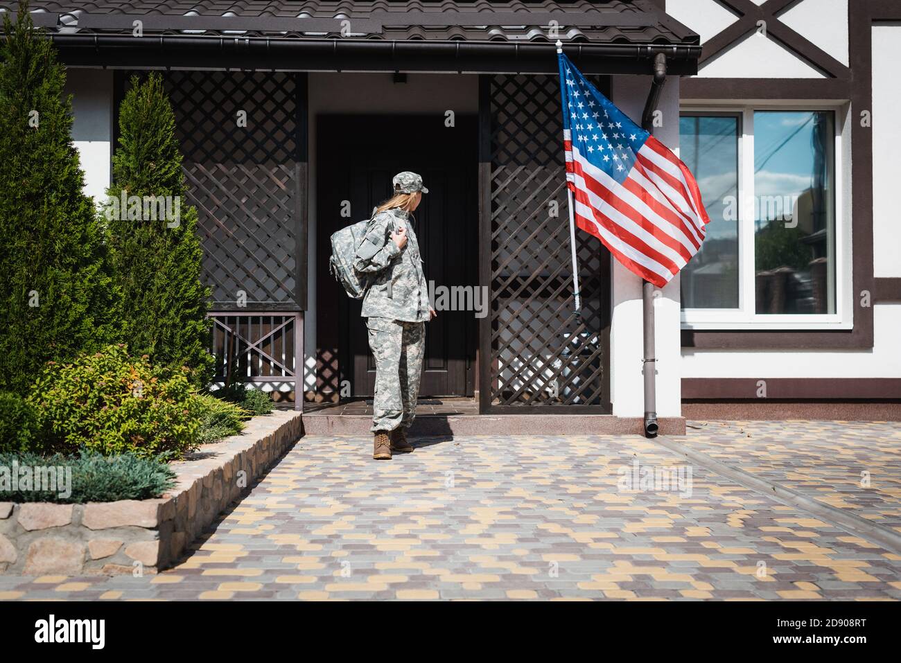 Military servicewoman with backpack leaving house, standing on threshold Stock Photo