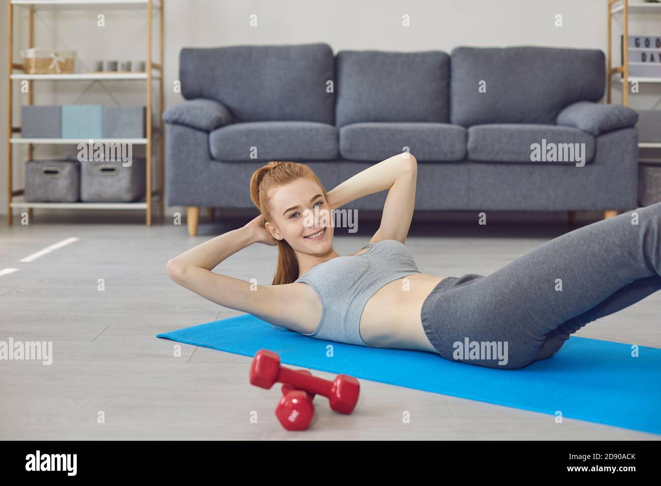 Smiling girl lying on fitness carpet, doing workout and looking at camera at home Stock Photo