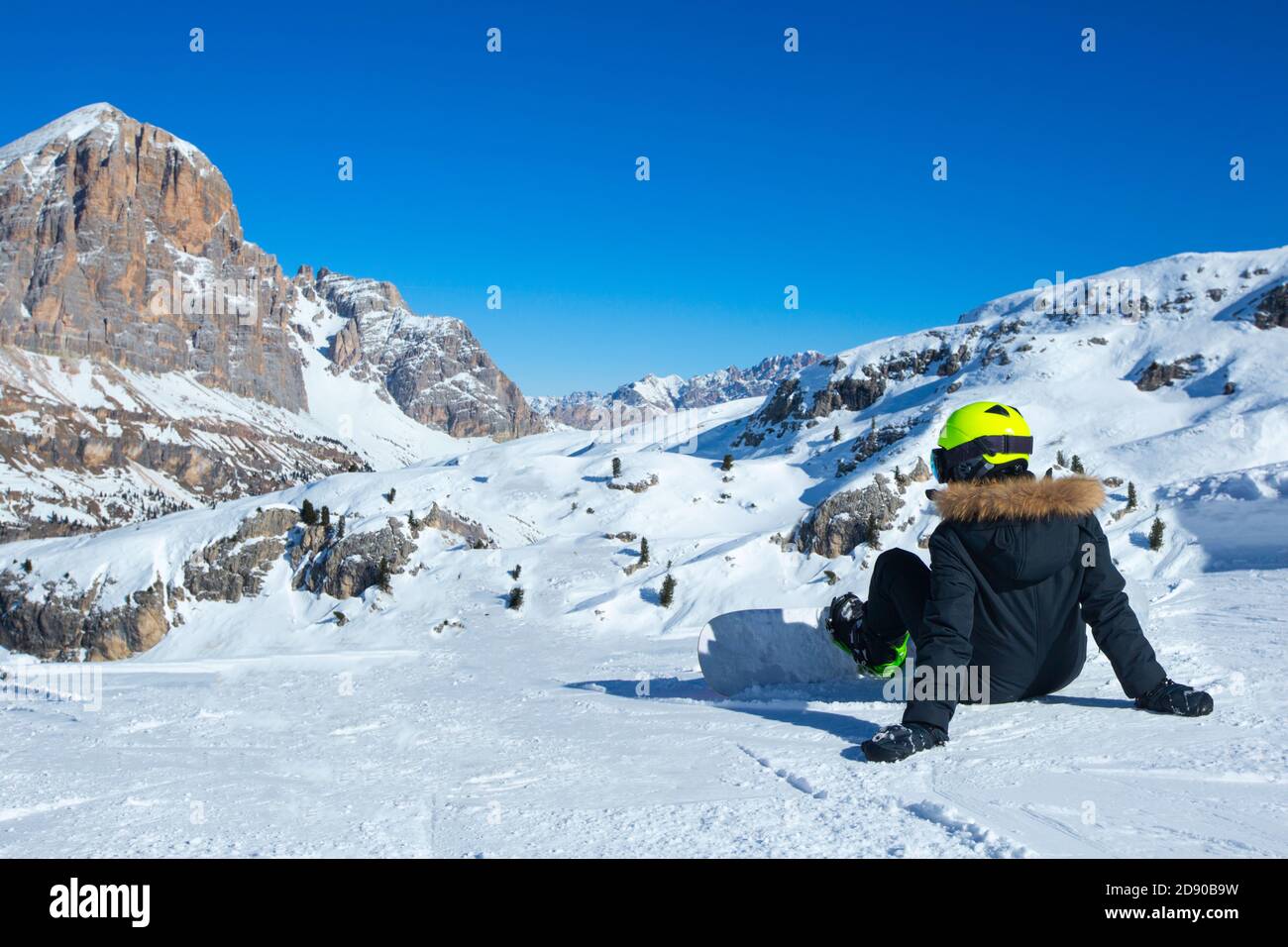 Rear view of female snowboarder sitting on ski slope at resort in Dolomites Italian Alps Stock Photo