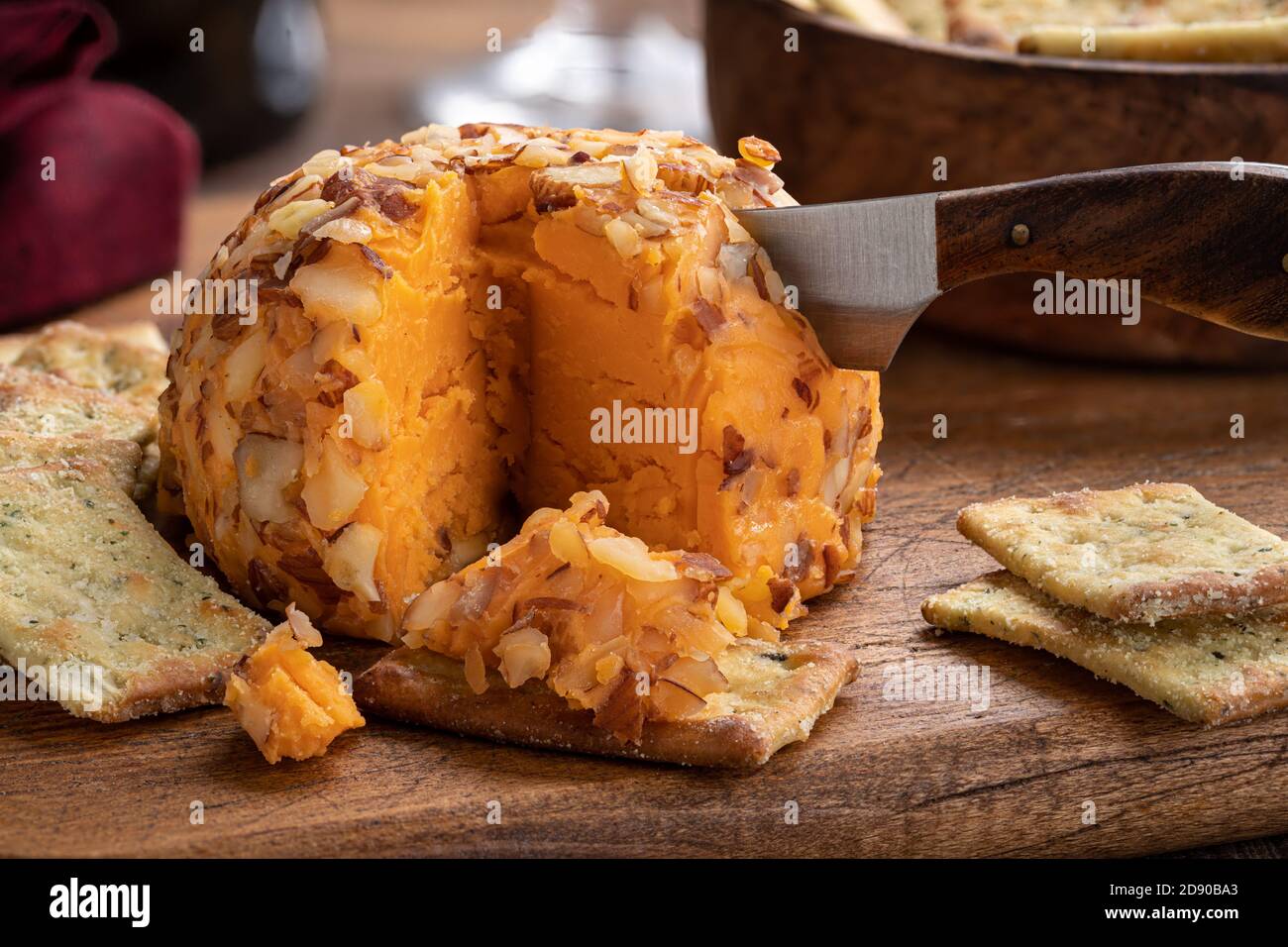 Closeup of a sliced cheddar cheese ball and crackers on a rustic cutting board Stock Photo
