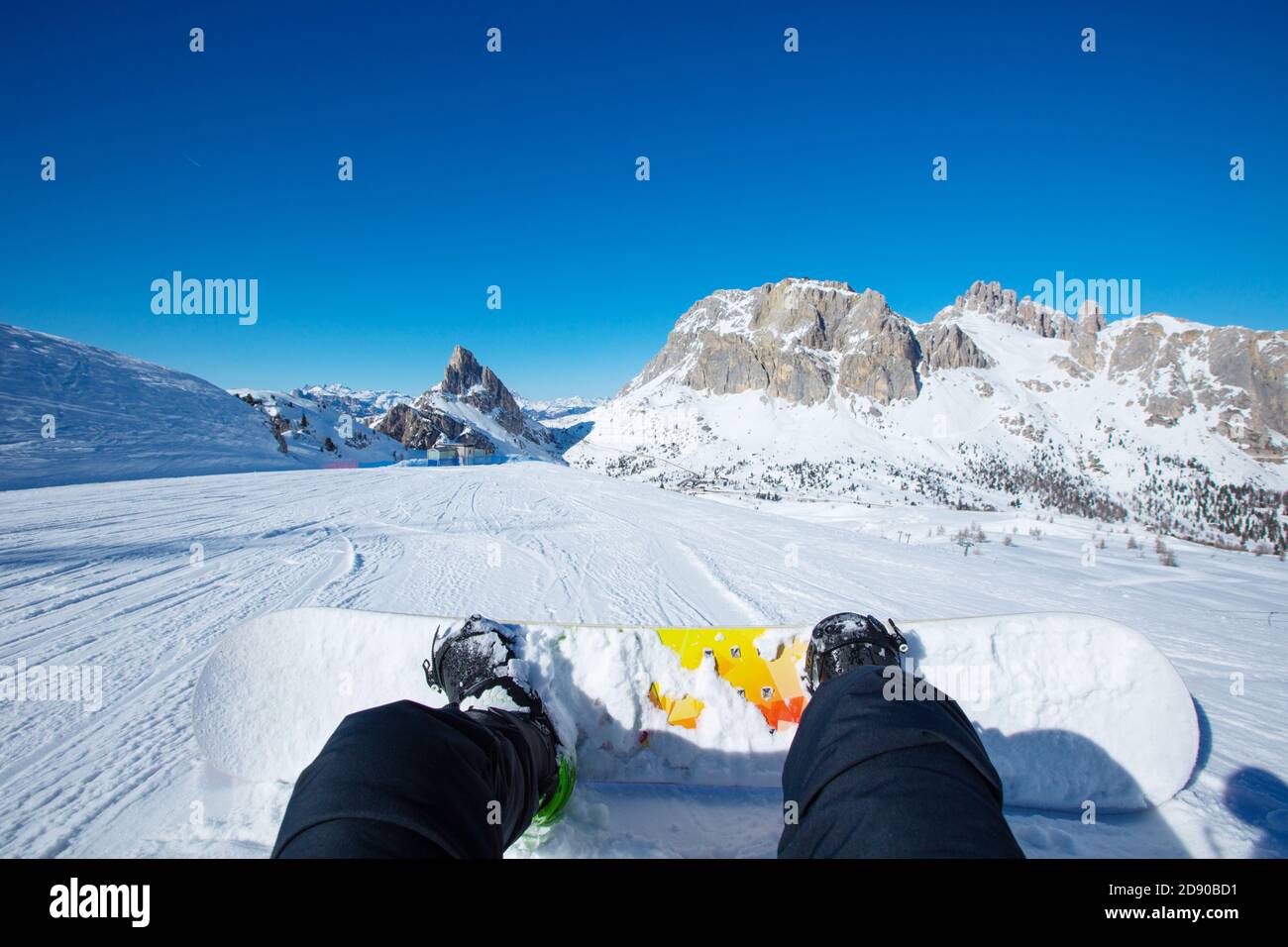 Snowboarder sitting on ski slope at resort in Dolomites Italian Alps view on legs and snowboard Stock Photo