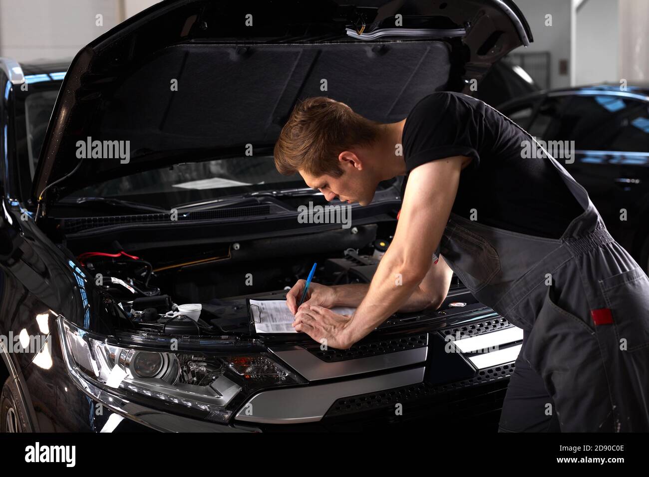 professional car mechanic is examining engine under the hood at auto repair  shop, make notes, checking notes in notebook Stock Photo - Alamy