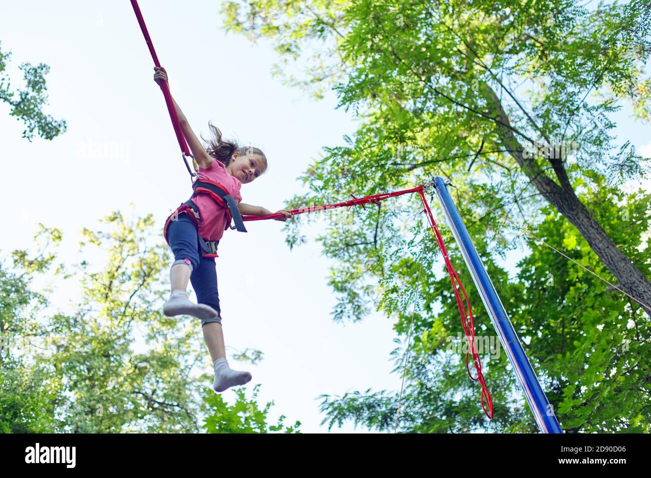 Child girl having fun jumping on trampoline with elastic ropes Stock Photo