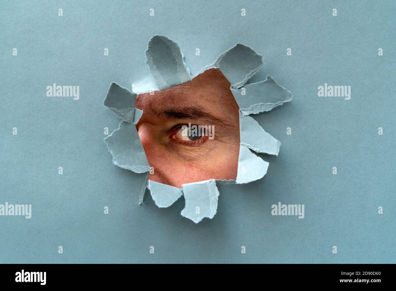 The human eye is watching us through a hole in a grey paper Stock Photo