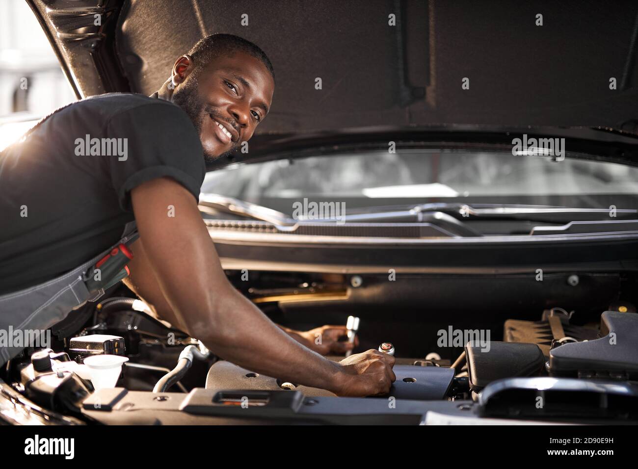 handsome guy repairing auto's hood, using tools. wearing unifrom