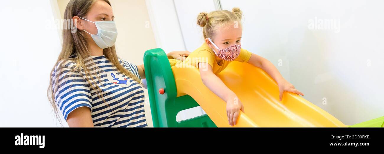 Toddler girl in child occupational therapy session doing playful exercises with her therapist during Covid - 19 pandemic, both wearing protective face Stock Photo