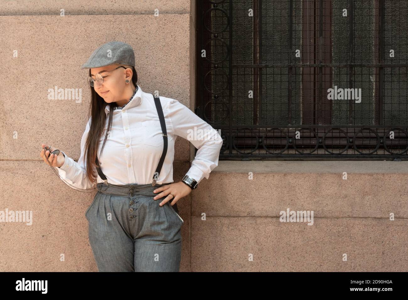 Cool vintage woman with suspenders looking at pocket watch against wall