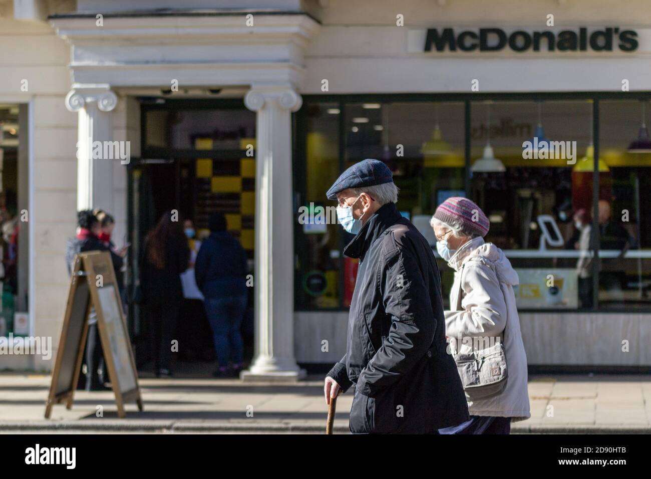 Elderly couple wearing face masks walk past Mcdonalds in Leamington Spa, Warwickshire as another month-long lockdown looms for the UK Stock Photo