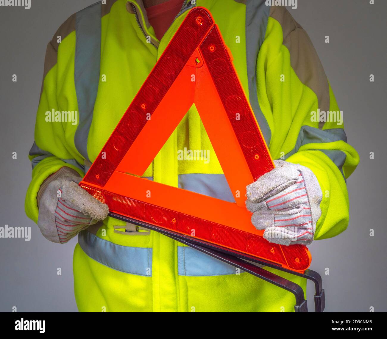 Closeup of a man wearing gloves and a fluorescent yellow, high visibility fleece safety jacket, holding an orange, reflective warning triangle. Stock Photo