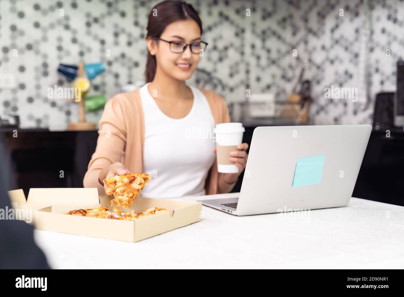 Asian woman work from home in the kitchen and eating delivery pizza take away food and take out coffee while city lockdown from coronavirus covid-19 p Stock Photo
