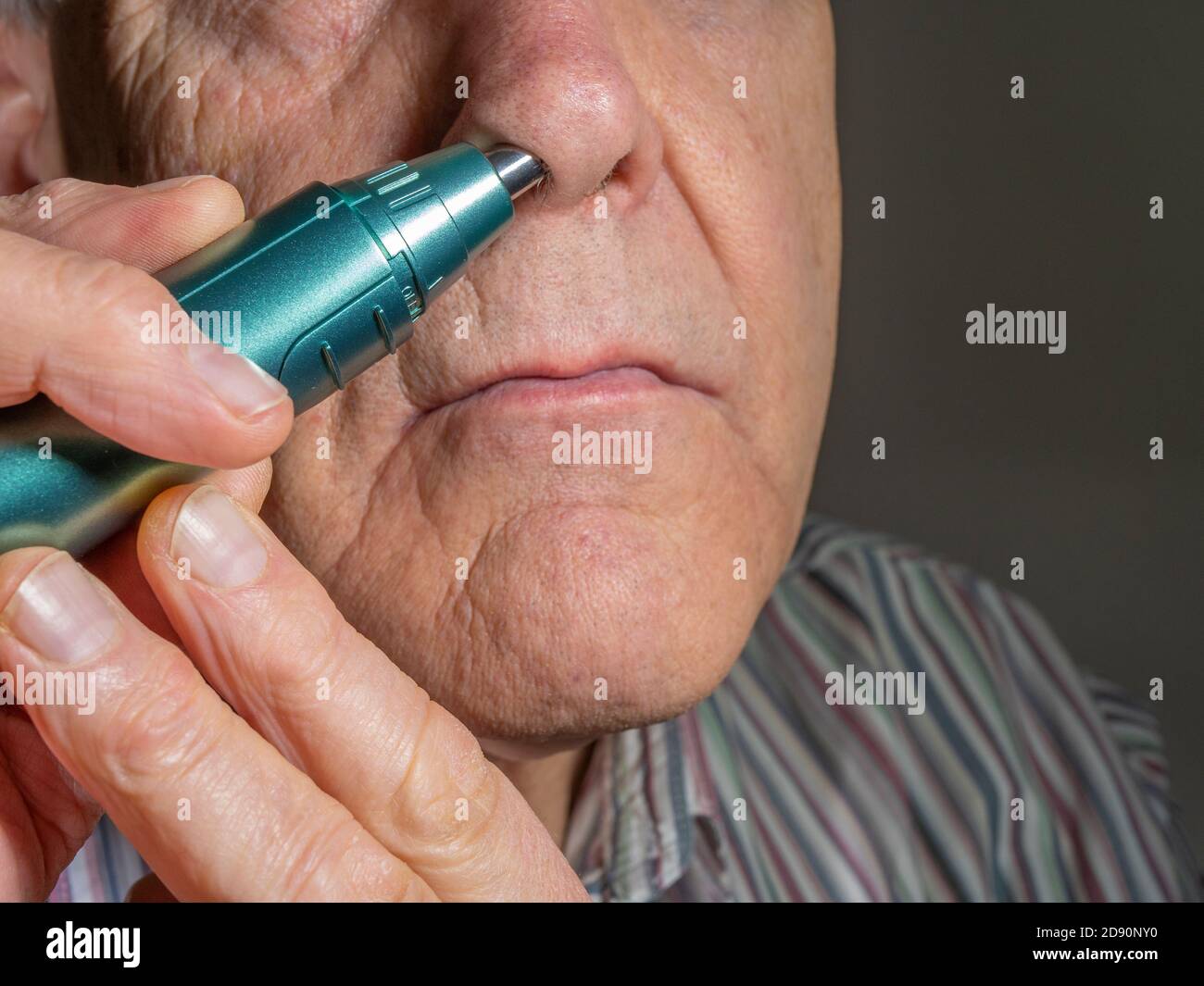 Closeup POV shot of an older man using a small, battery powered hand held trimmer to remove excess hair from a nostril. Stock Photo