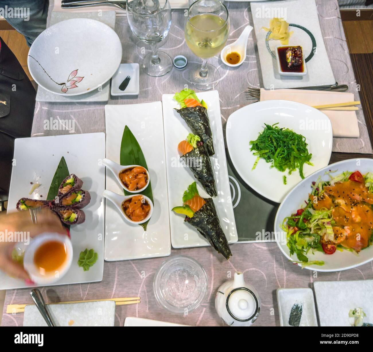 flat lay of a Japanese and Chinese fusion table full of delicious dishes. Black Uramaki of salmon, Temaki rice cones, fresh salmon tartar, seaweed Stock Photo
