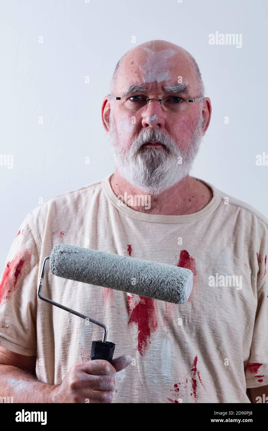Senior man looking slightly miserable, having just finished painting a room. Stock Photo