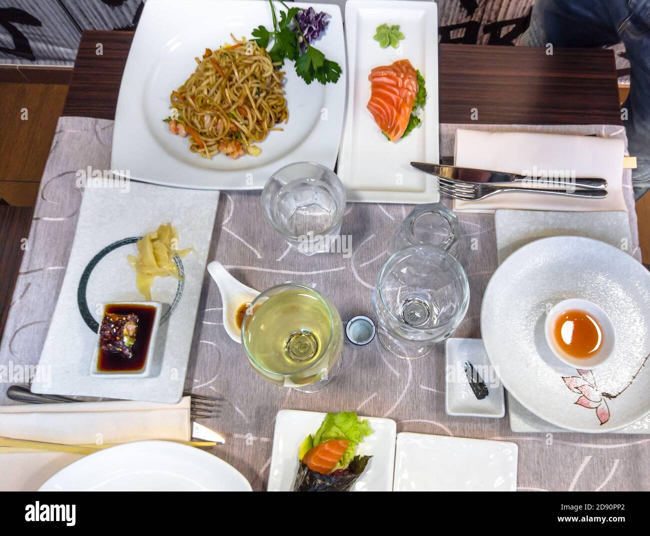 Japanese dinner on a table full of delicious dishes. fresh salmon sushi, shrimps spaghetti and white wine. Stock Photo