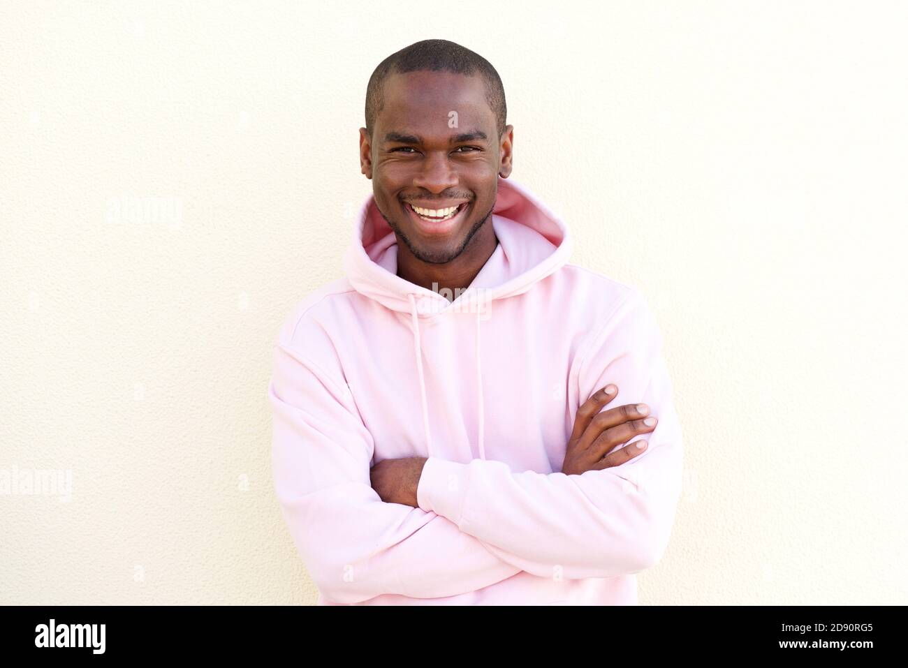 Portrait of cool young black man smiling with arms crossed by light ...