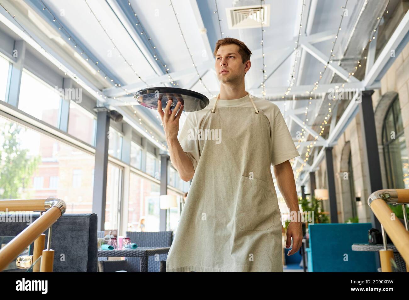 confident caucasian male waiter in apron holding tray in hands, serve the client in restaurant, going to give food to customer Stock Photo