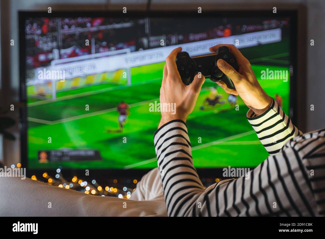 Close up male hands playing video game football soccer on console. gamer man with gamepad controller holding Wireless joystick sitting on pouf at nigh Stock Photo