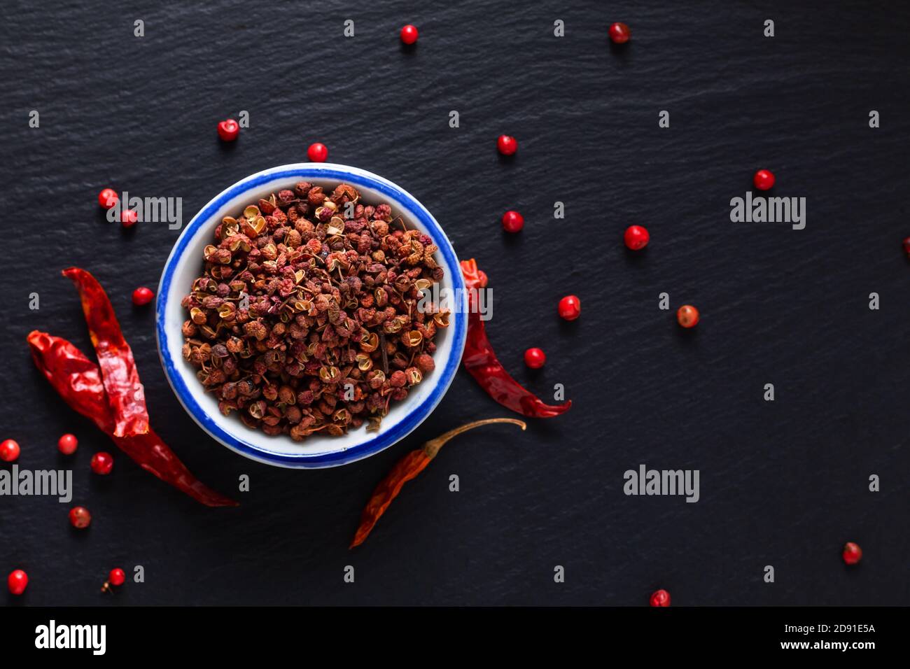 Food hot and spicy ingredients concept Sichuan, Szechuan, Szechwan pepper in small ceramic bowl on black slate stone board with copy space Stock Photo