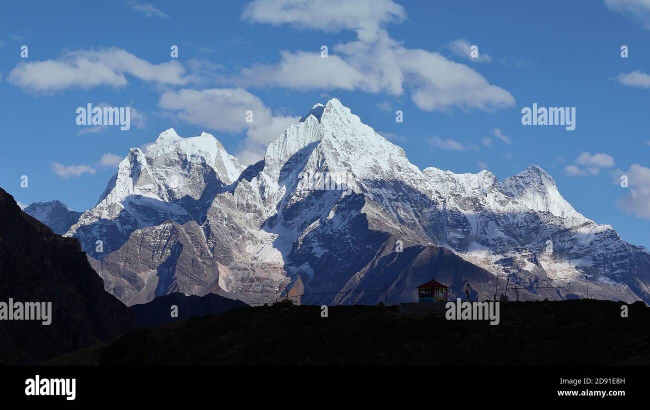 Beautiful panorama of majestic mountain Thamserku (peak: 6,623 m) with the silhouettes of a small temple and Buddhist prayer flags in foreground. Stock Photo