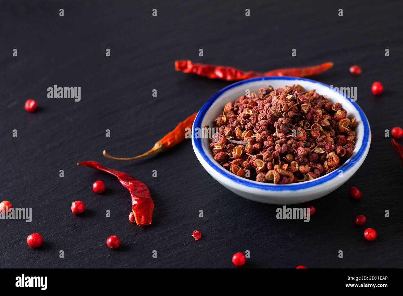 Food hot and spicy ingredients concept Sichuan, Szechuan, Szechwan pepper in small ceramic bowl on black slate stone board with copy space Stock Photo