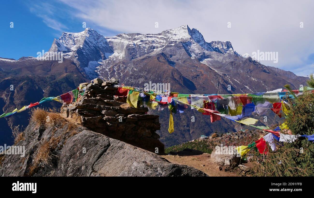 Multi-colored Buddhist prayer flags attached to a pile of stones flying in the wind above village Namche Bazar, Khumbu, Himalayas, Nepal. Stock Photo