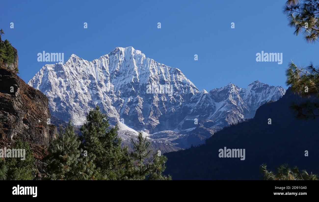 Majestic mountain Thamserku (6,623 m) in the Himalayas seen from Mount Everest Base Camp Trek near Manjo, Nepal framed by coniferous trees. Stock Photo