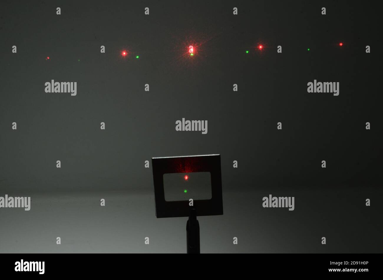 In a darkened room, two laser beams from a source under the camera, hits an optical grid and an interference pattern apppears on the wall in the backg Stock Photo
