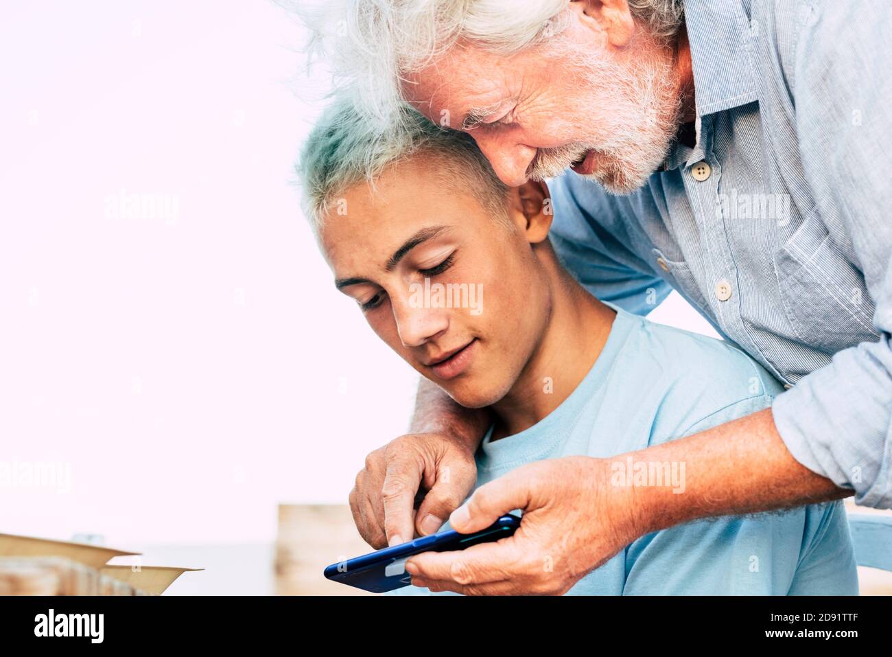 Portrait of young and old people grandfather and grandson together using a modern smart phone - family and friends concept with teenager and senior ma Stock Photo