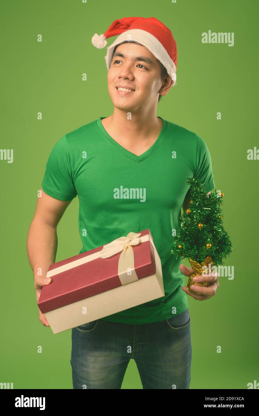 Young handsome Filipino man ready for Christmas against green background Stock Photo