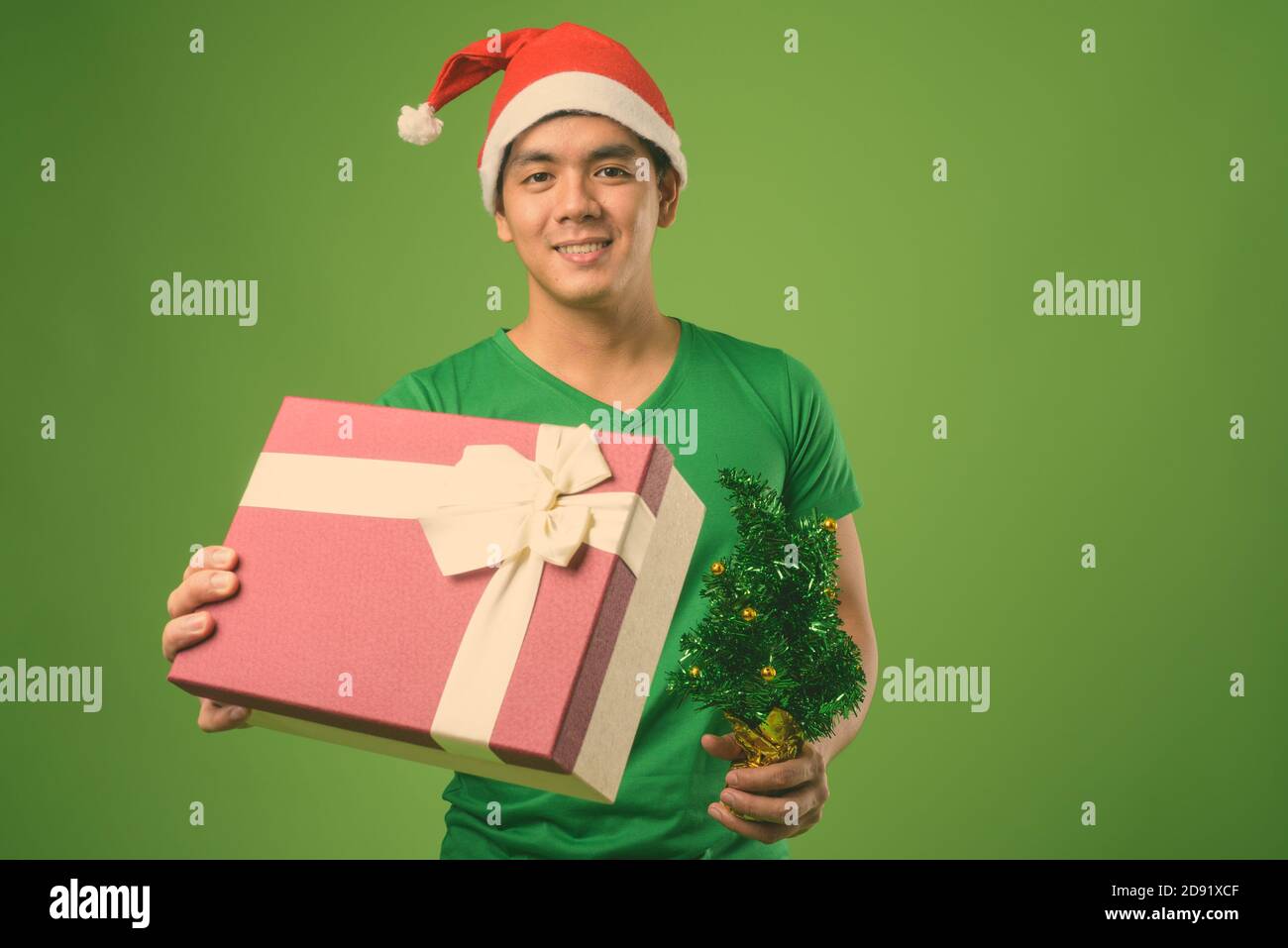 Young handsome Filipino man ready for Christmas against green background Stock Photo