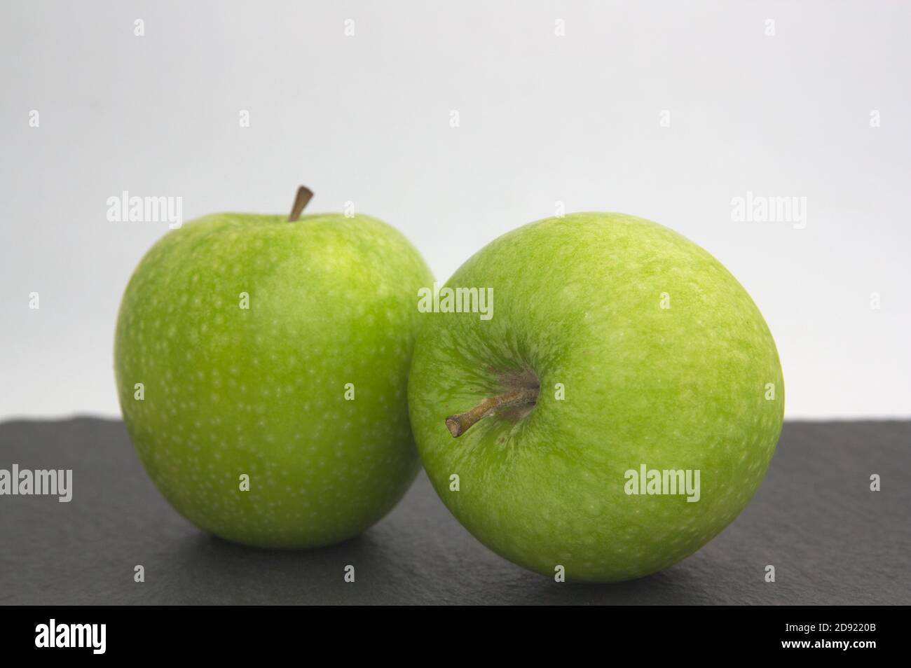 A pair of green apples of golden type on a black surface and white background with copy space Stock Photo