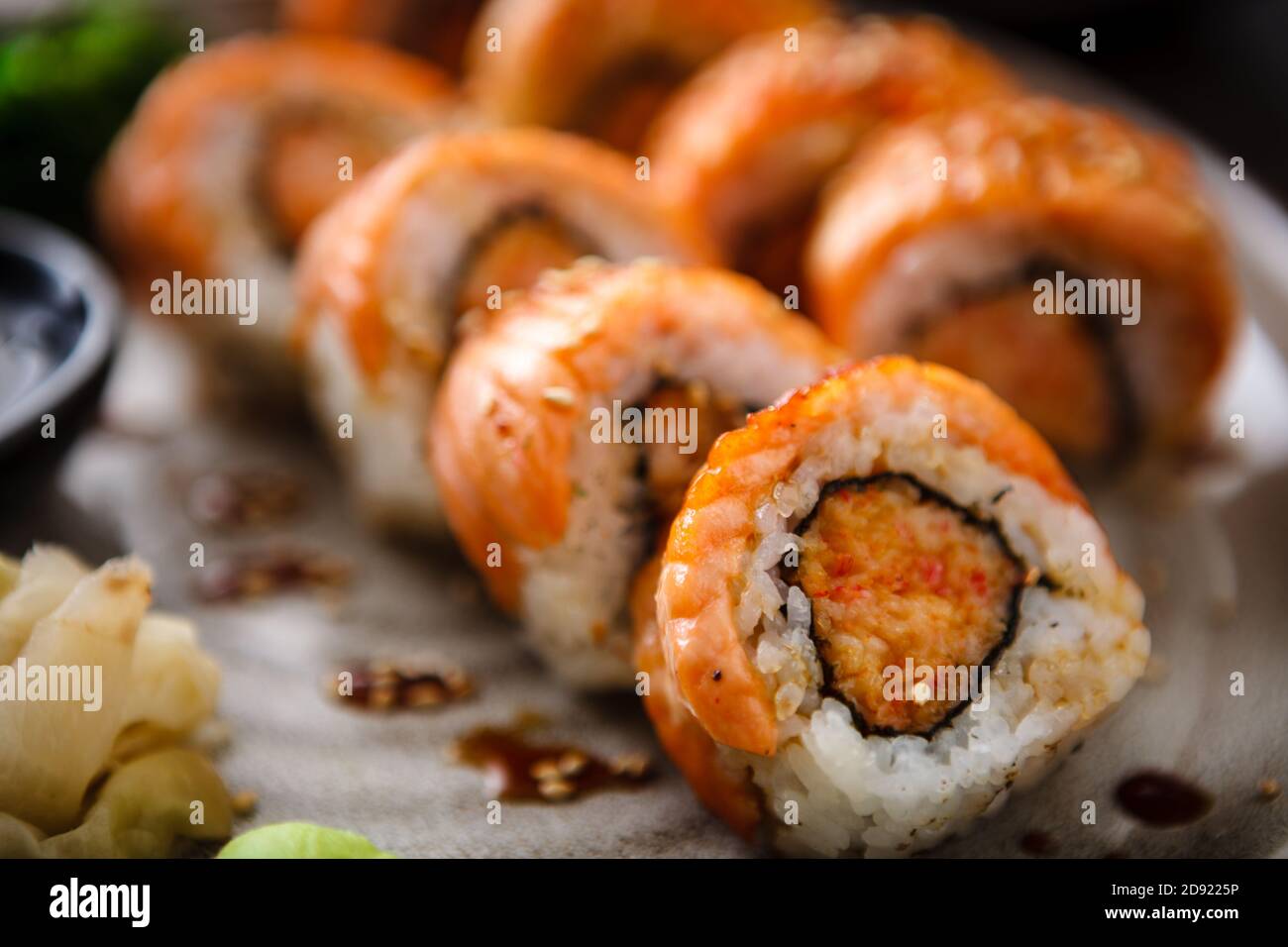 Baked sushi maki rolls with salmon, crab and spicy sauce on a plate with chopsticks, soy sauce, wasabi and ginger. Japanese traditional fish food Stock Photo