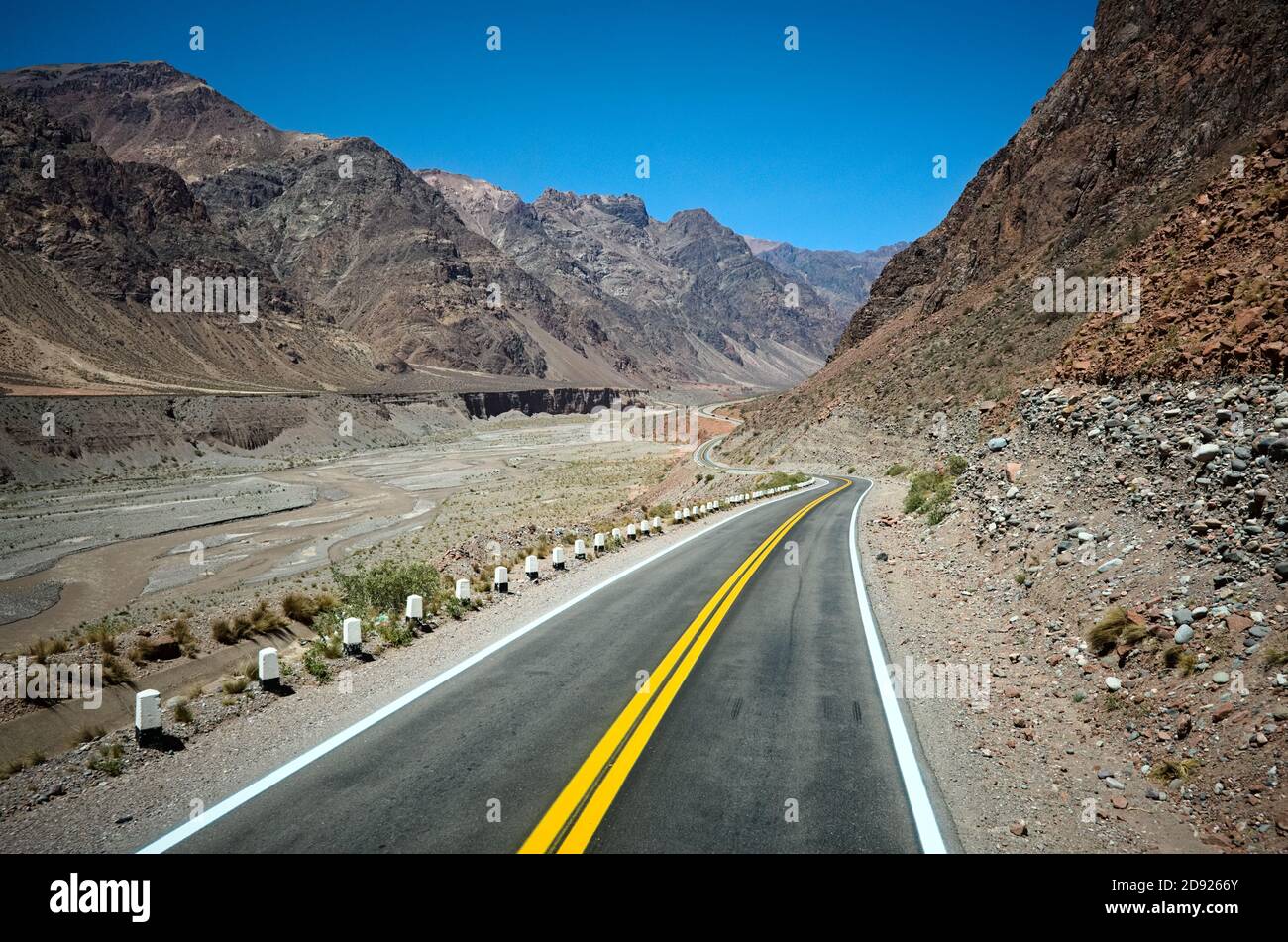 Highway road in the Andes mountains along canyon river. Empty road in arid climate as desert with rocky terrain. Curved road with yellow dividing line Stock Photo