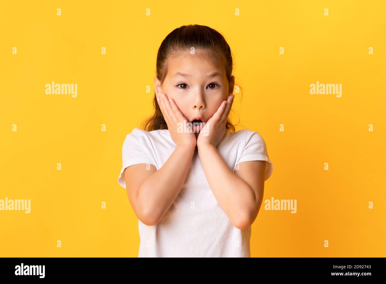 Asian kid with open mouth touching cheeks in excitement Stock Photo Alamy