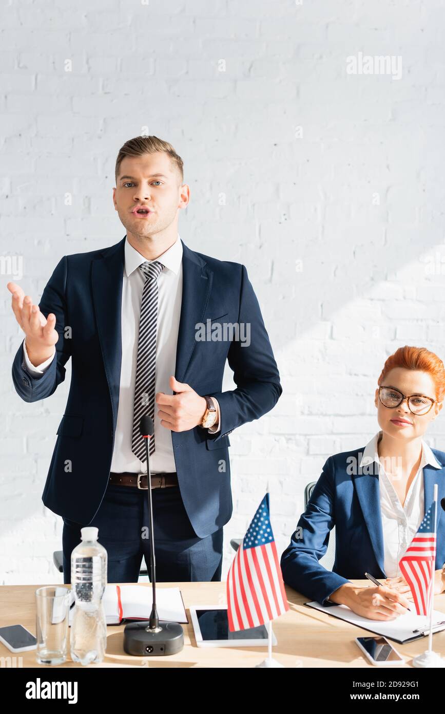 Confident politician gesturing, while talking, standing near smiling