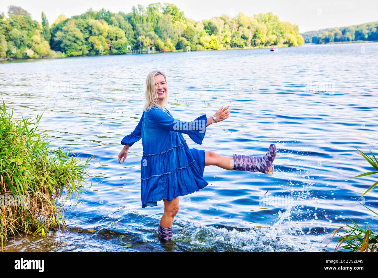 blond woman in a blue dress standing in water with rubber boots Stock Photo