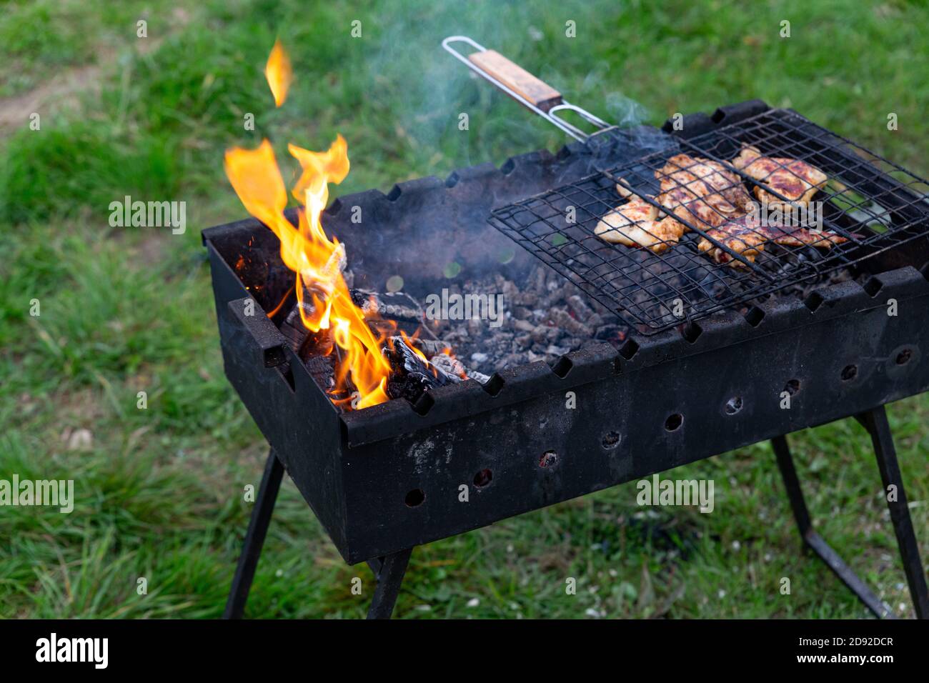 Meat is grilled on charcoal grill. Coals smolder in a brazier with smoke focus on fire. Outdoor cooking. Meeting with friends, picnic, weekend. Evenin Stock Photo