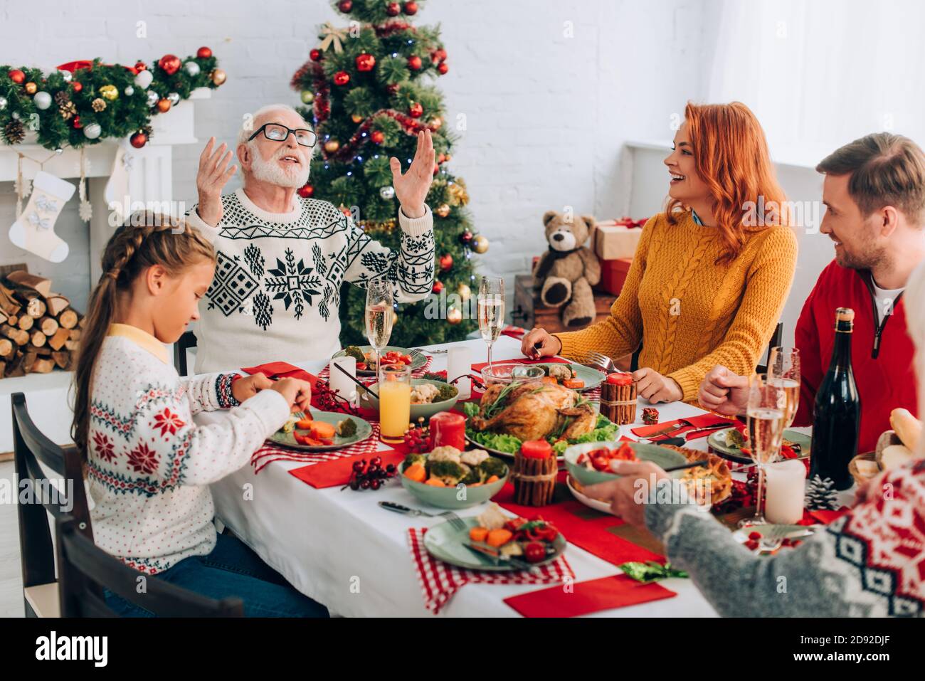 Family sitting at festive table with thanksgiving dinner near fireplace