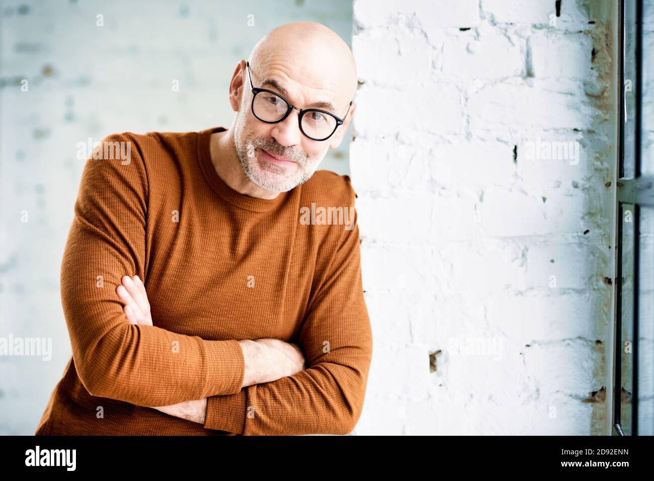 Portrait shot of curious man with beard and eyewear standing at the wall and looking at camera. Stock Photo